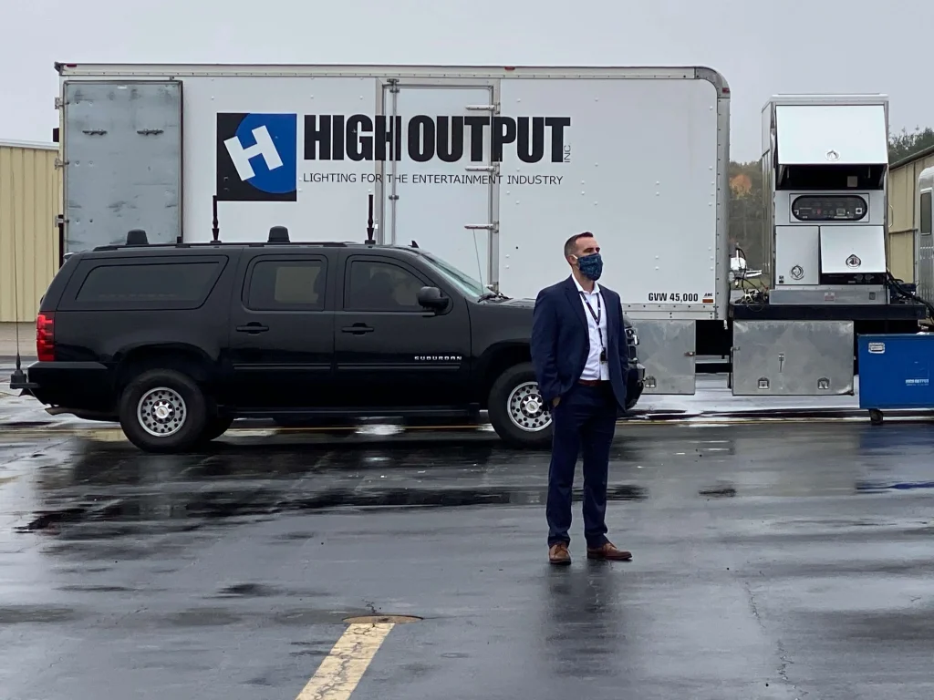 Man in suit in from of High Output truck
